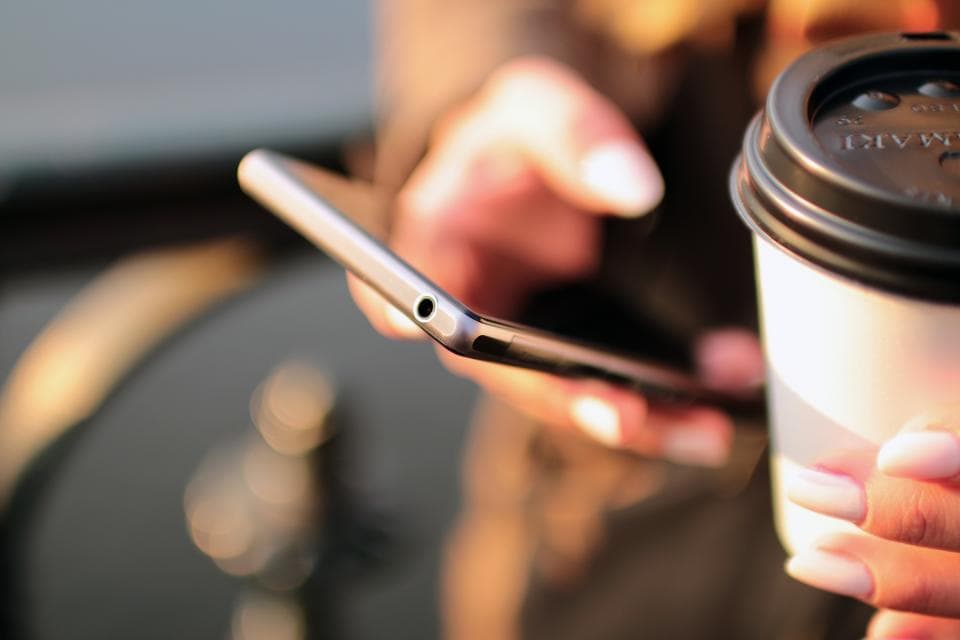 A hand holding a smartphone beside a takeaway coffee cup.