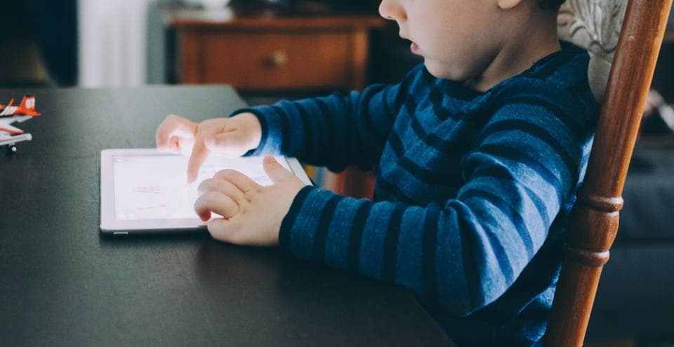 A child in a striped sweater tapping a tablet on a table.