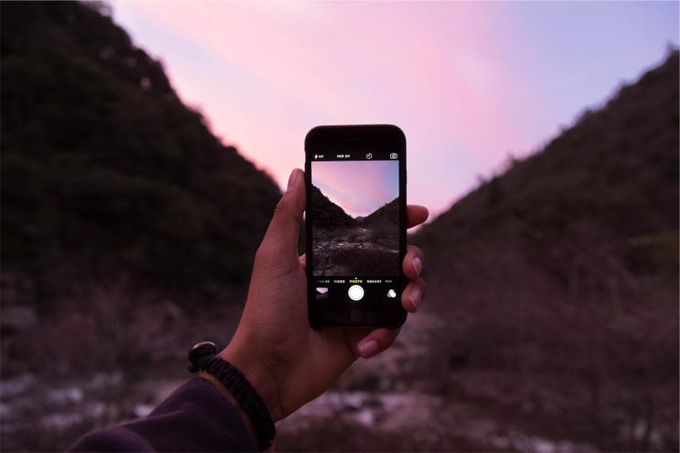A phone held up to photograph a mountain valley under a pink evening sky.